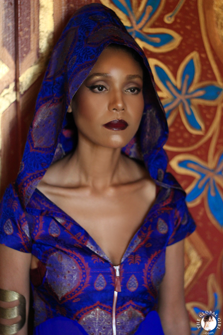 The Global Girl Editorials: Ndoema sports a silk hooded dress, tribal upper arm bracelet against vibrant gold Moroccan frescoes.