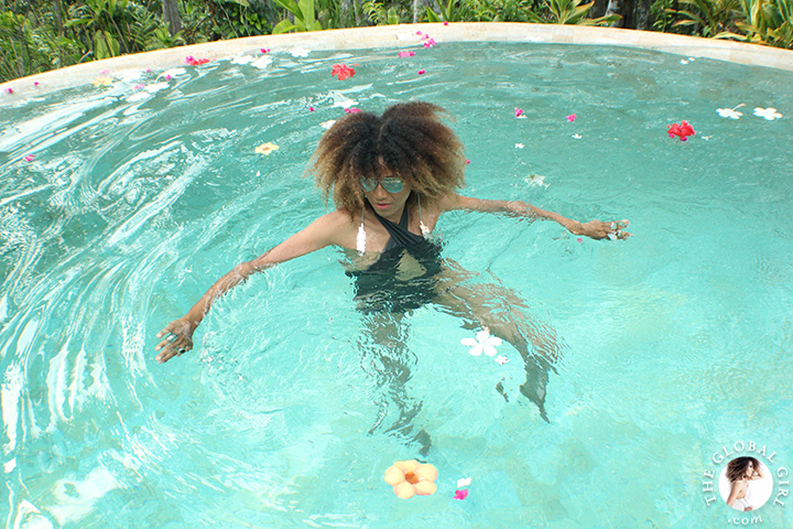 The Global Girl Travels: Ndoema lounges poolside in a cross halter one-piece swimsuit and silver aviator mirrored sunglasses at Glamping Hub's eco-chic tents in Ubud, Bali. The suite's private jungle-flanked infinity pool provides utmost serenity.